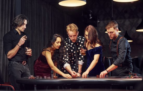 Standing by the table. Group of elegant young people that playing poker in casino together.